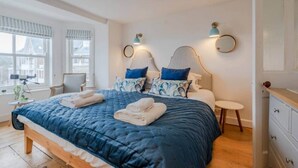 A modern bedroom with a large bed, two bedside tables, a small round table, and a dresser.