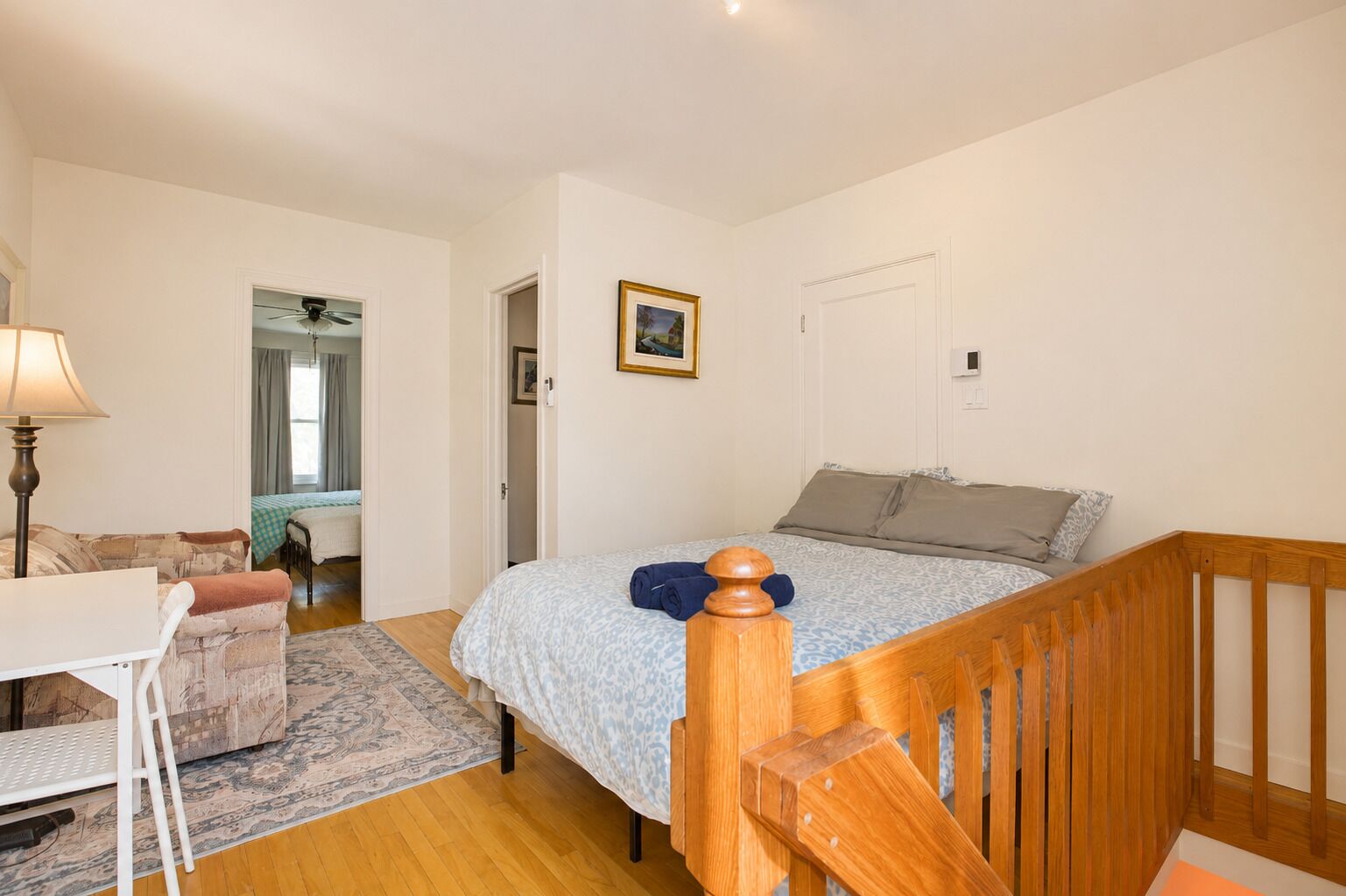 A bedroom with a bed, a desk, a chair, a wooden headboard, and a door.
