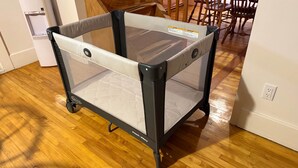 A portable playpen with wheels, a water dispenser, and a dining area with wooden chairs and a table. - Chez Claude appartement millésimé-free parking (Québec City)
