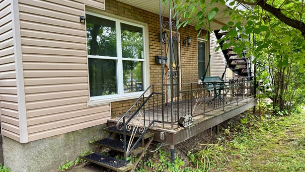 A two-story house with a covered porch, a small outdoor seating area, and a metal staircase leading to the porch. - Chez Claude appartement millésimé-free parking (Québec City)