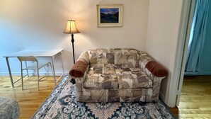 A living room with a patterned sofa, a small table, a floor lamp, and a framed picture on the wall. - Chez Claude appartement millésimé-free parking (Québec City)