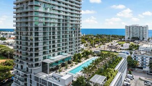 A multi-story hotel with a pool, surrounded by greenery and a view of the sea.
