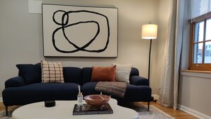 A living room with a dark blue sofa, a white coffee table, and a large abstract painting on the wall. - Spacious 1BD With Balcony (Philadelphia)