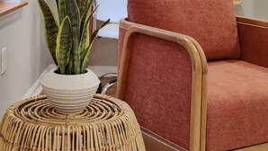 A room with a round mirror on the wall, a potted plant, a wicker stool, and a red upholstered chair. - Spacious 1BD With Balcony (Philadelphia)