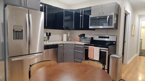 A modern kitchen with stainless steel appliances, black cabinets, and a round dining table with chairs. - Spacious 1BD With Balcony (Philadelphia)