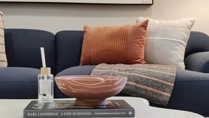 A modern living room with a dark blue sofa, a white coffee table, and a book titled 'A Life in Houses'. - Spacious 1BD With Balcony (Philadelphia)