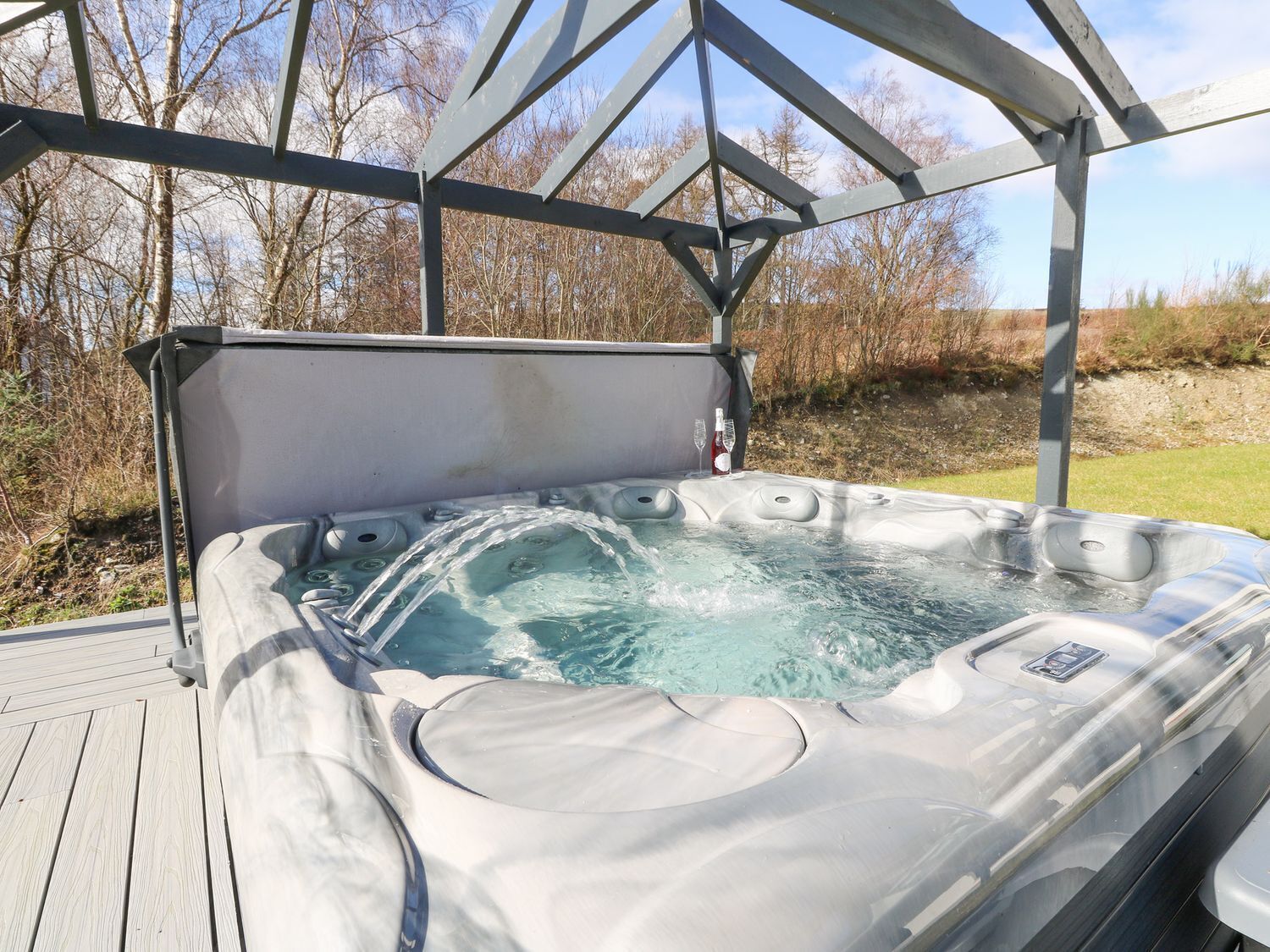 A hot tub with a metal frame and a canopy, surrounded by a wooden deck and a grassy area.