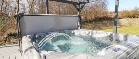 Un bain à remous doté d’une structure métallique et d’un auvent, entouré d’une terrasse en bois et d’une zone herbeuse.