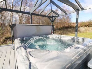Un bain à remous doté d’une structure métallique et d’un auvent, entouré d’une terrasse en bois et d’une zone herbeuse.