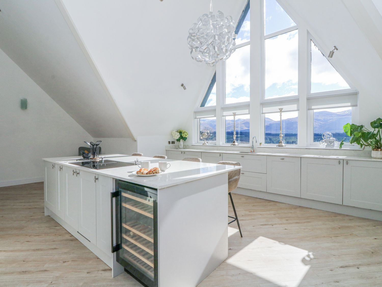 Una cocina moderna con una isla grande, armarios blancos y vistas a montañas a través de amplios ventanales.