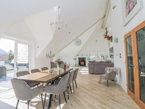 Un loft spacieux avec un plafond haut, un coin repas avec une longue table et des chaises, une cheminée et un salon confortable avec un canapé et une décoration représentant une tête de cerf.