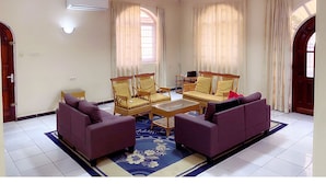 A spacious living room with a sofa set, a coffee table, and a small table with chairs. - Paramaribo Villa for 8 People, 4 Bedrooms, Full Air Conditioning, Near the Mall, Including Housekeeping Service! (Paramaribo)