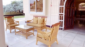 A covered patio area with wicker furniture, a glass table, and a large arched window. - Paramaribo Villa for 8 People, 4 Bedrooms, Full Air Conditioning, Near the Mall, Including Housekeeping Service! (Paramaribo)