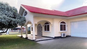 A two-story building with a red roof, a covered entrance with arched doorways, and a garage. - Paramaribo Villa for 8 People, 4 Bedrooms, Full Air Conditioning, Near the Mall, Including Housekeeping Service! (Paramaribo)