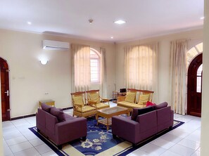 A spacious living room with a sofa set, a coffee table, and a small table with chairs. - Paramaribo Villa for 8 People, 4 Bedrooms, Full Air Conditioning, Near the Mall, Including Housekeeping Service! (Paramaribo)