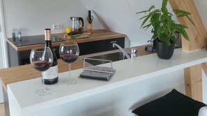 Eine moderne Küche mit weißem Arbeitsplatz, zwei Weingläsern, einer Weinflasche, einer Kaffeemaschine und einer Topfpflanze.