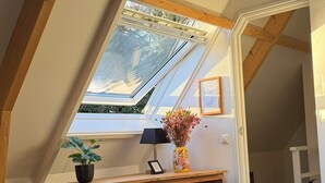 Ein modernes Schlafzimmer im Loft-Stil mit Dachfenster, Holzbalken, Schreibtisch, Stuhl und einer Topfpflanze.