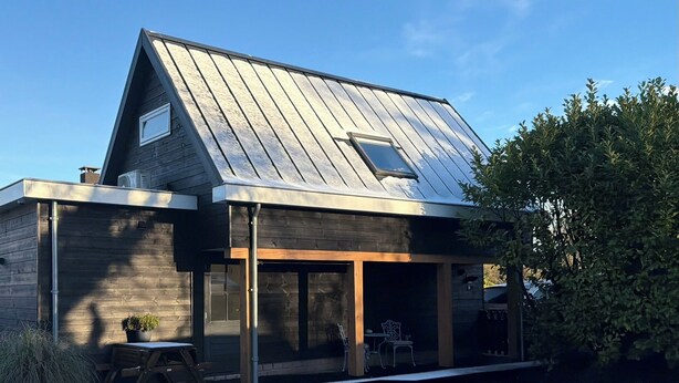 Ein modernes Haus mit geneigtem Dach, großen Fenstern und einer überdachten Veranda.