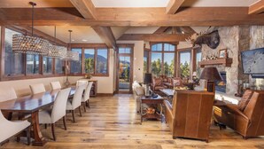 Un salon spacieux doté d’un plancher en bois, de grandes fenêtres, d’une cheminée et d’une tête de cerf fixée au mur.