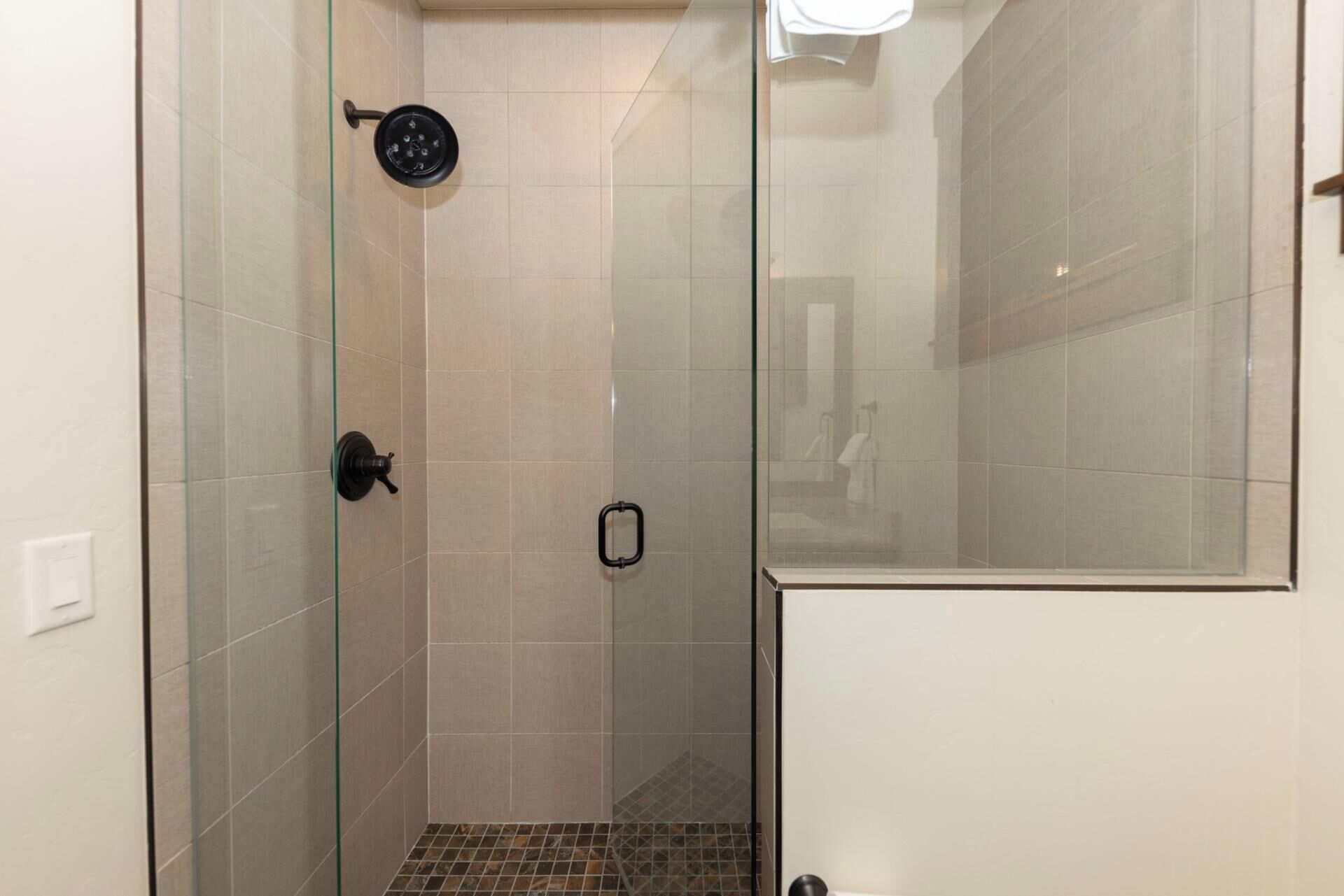 Un espace douche doté d’une porte en verre, de murs carrelés et d’un pommeau de douche.