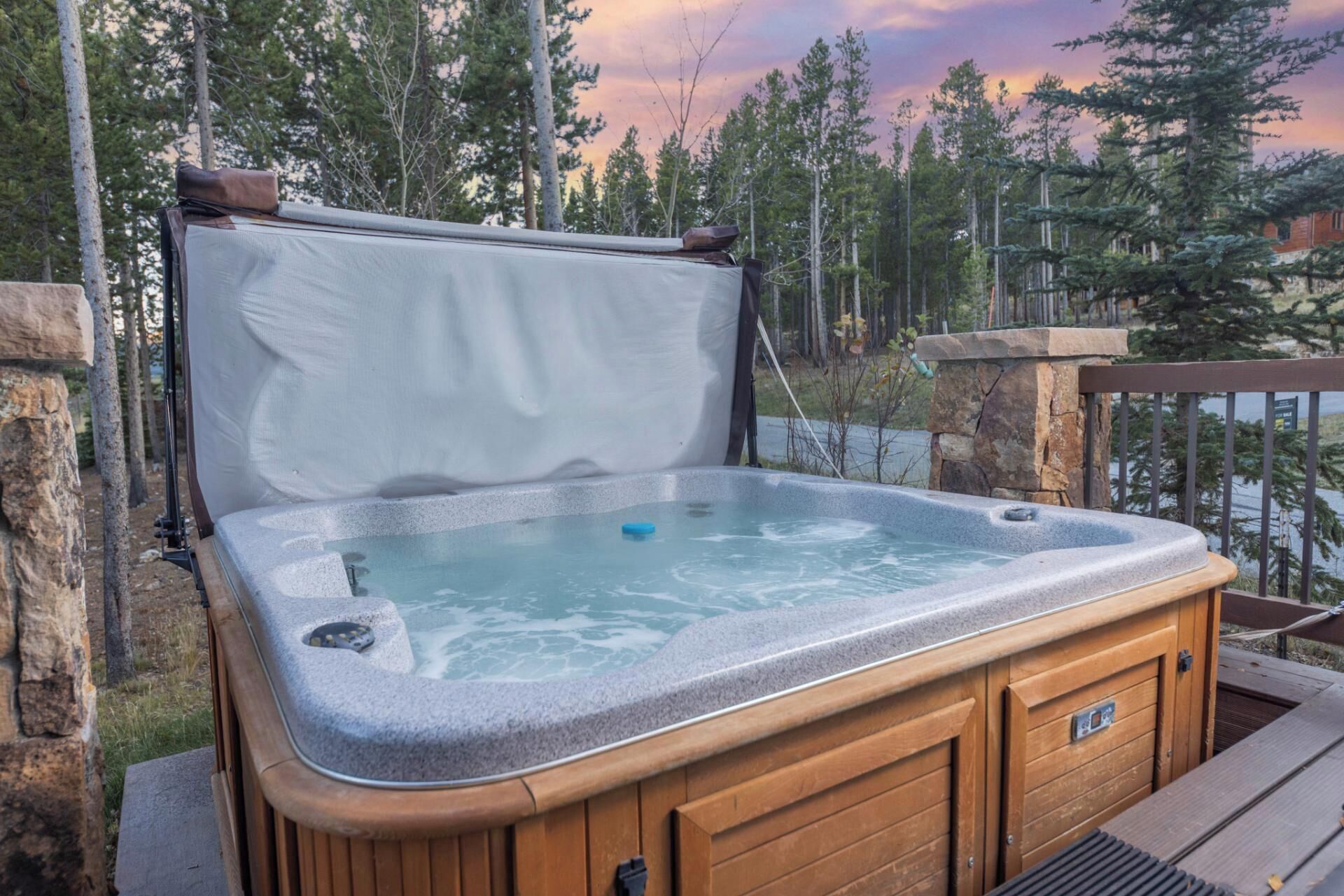 Un jacuzzi con muelle de madera y paredes de piedra, rodeado de árboles y vistas a un lago.