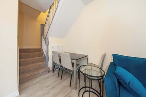 A compact living space with a staircase, a dining table with chairs, a glass-top coffee table, and a blue sofa. - Bright 2BR at Kilmainham Gaol-reduced prices (Dublin)