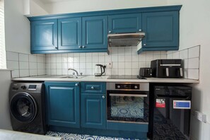 A compact kitchen with teal cabinets, a washing machine, a dishwasher, and a microwave. - Bright 2BR at Kilmainham Gaol-reduced prices (Dublin)