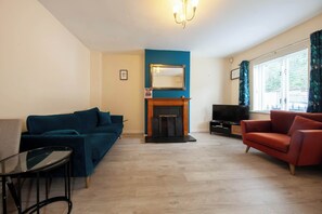 A living room with a blue sofa, a red armchair, a glass coffee table, a fireplace, and a TV. - Bright 2BR at Kilmainham Gaol-reduced prices (Dublin)