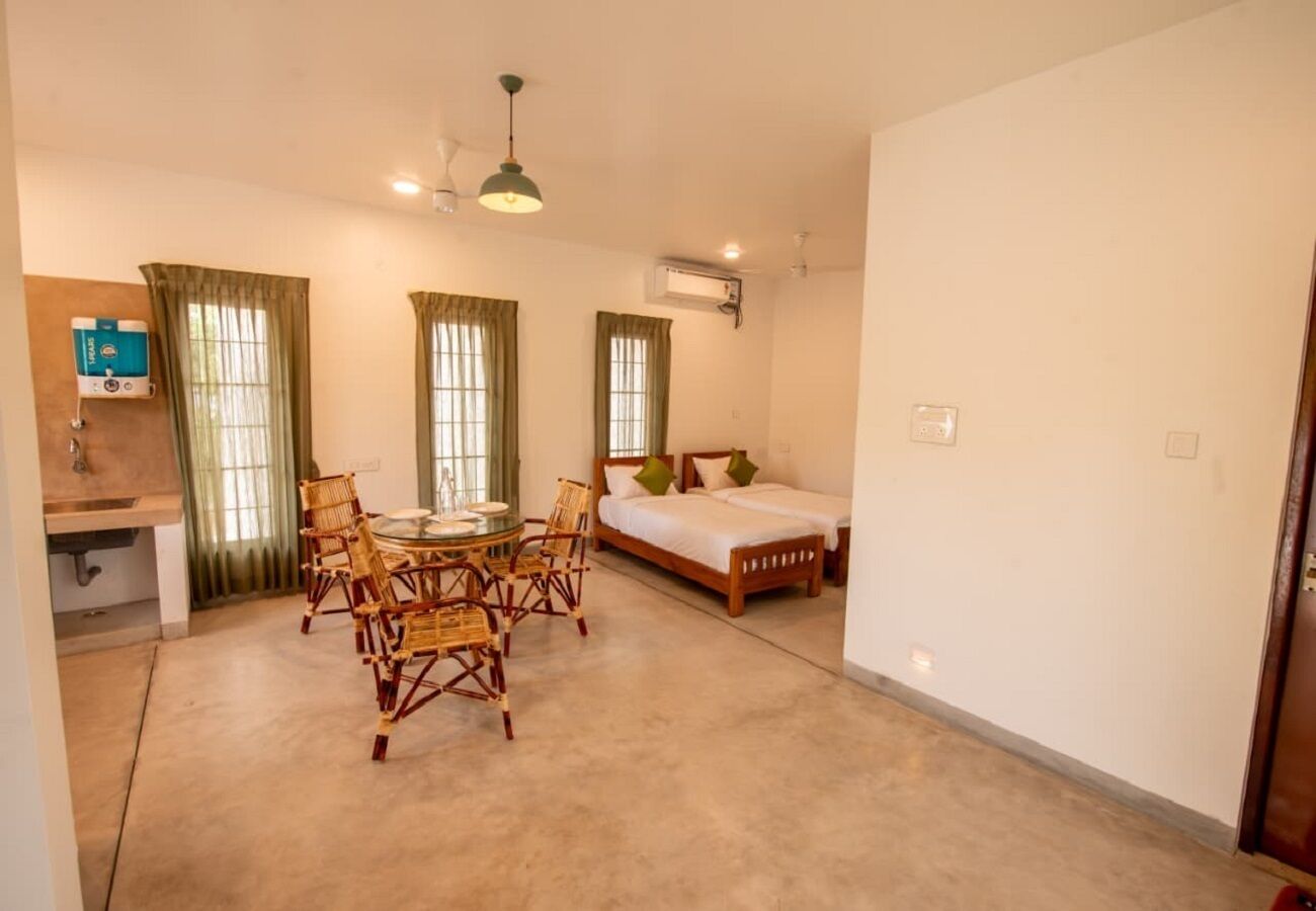 A room with a bed, a round table with chairs, a window with curtains, and an air conditioning unit.