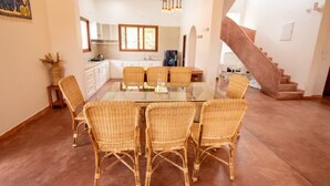 A spacious dining area with a glass table and wicker chairs, a kitchen in the background, and a staircase leading to another level. - Shambala Resort (Bommayapalayam)