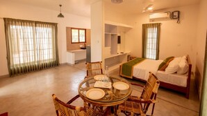 A hotel room with a bed, a desk, a chair, a dining table with plates, and a window with curtains. - Shambala Resort (Bommayapalayam)