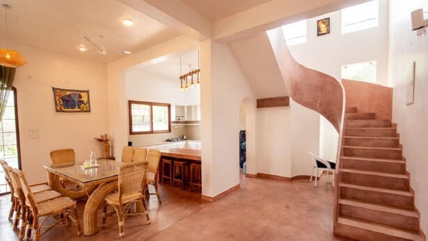 A spacious living area with a dining table and chairs, a kitchen in the background, and a spiral staircase. - Shambala Resort (Bommayapalayam)