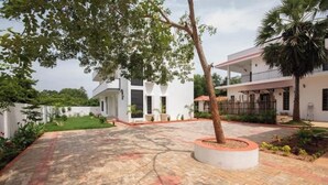 A courtyard with a paved walkway, a tree planter, and a white building with balconies. - Shambala Resort (Bommayapalayam)