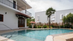 A swimming pool with a curved edge, surrounded by a wooden fence and plants. - Shambala Resort (Bommayapalayam)