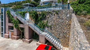 Un bâtiment moderne doté d’un mur de soutènement en pierre, d’un escalier avec des rampes en métal et d’une voiture rouge garée devant.