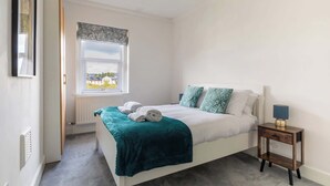 A bedroom with a bed, a bedside table, a window, and a radiator. - Refurbished Modern 2BD Flat, Lower Oldfield Park (Bath and North East Somerset)