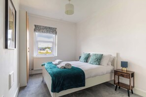 A bedroom with a bed, a bedside table, a window, and a radiator.
