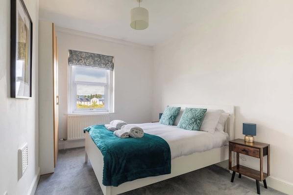 A bedroom with a bed, a bedside table, a window, and a radiator.