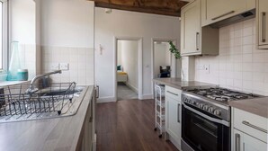 A modern kitchen with a central island, stainless steel appliances, and a wooden ceiling beam. - Refurbished Modern 2BD Flat, Lower Oldfield Park (Bath and North East Somerset)