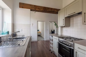 A modern kitchen with a central island, stainless steel appliances, and a wooden ceiling beam.