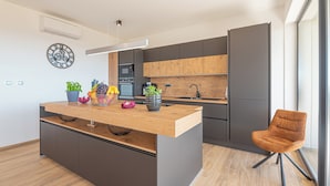 Een moderne keuken met een centraal eiland, donkere kastjes en een houten aanrecht.