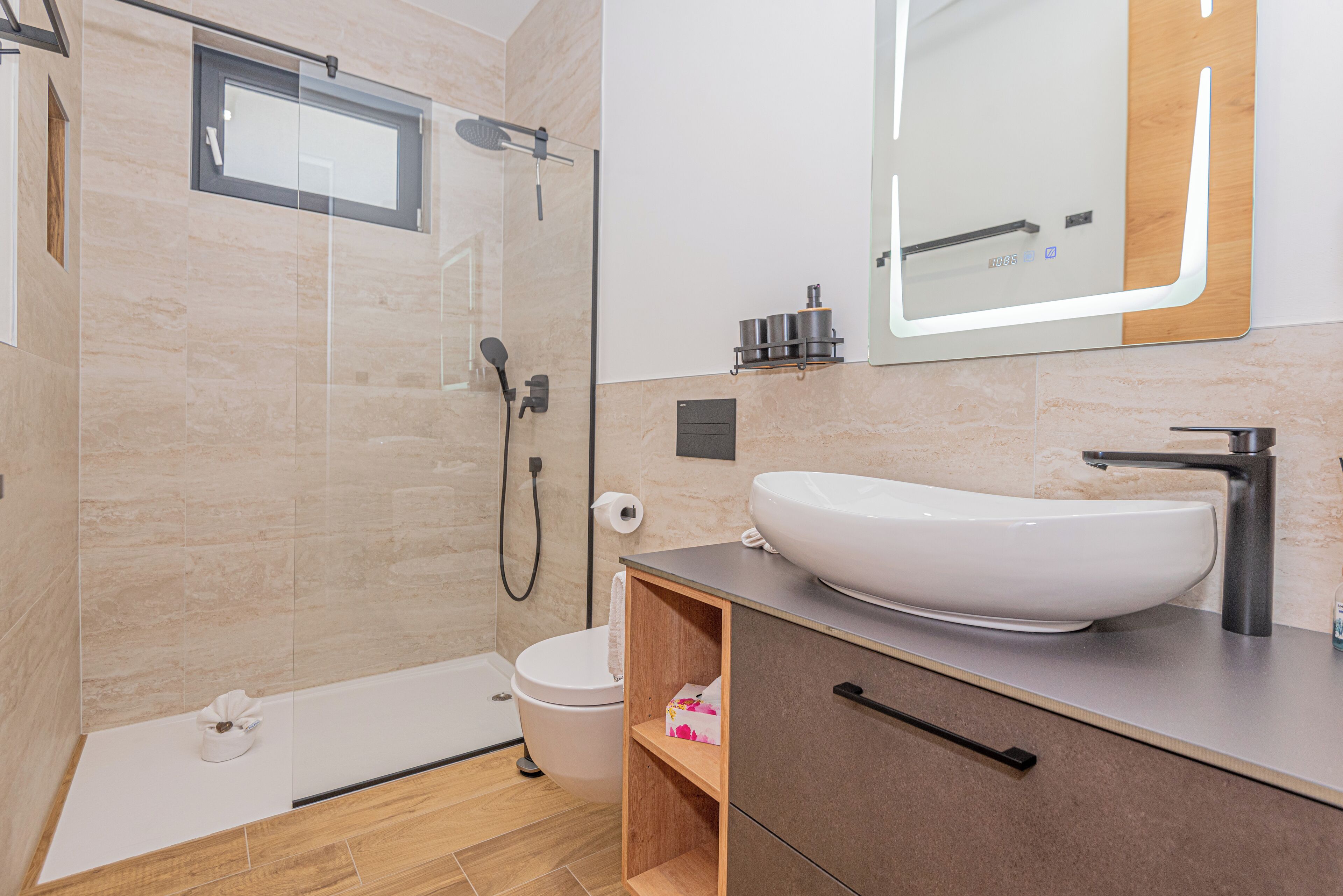 A modern bathroom with a glass-enclosed shower, a white sink, and a wooden vanity.