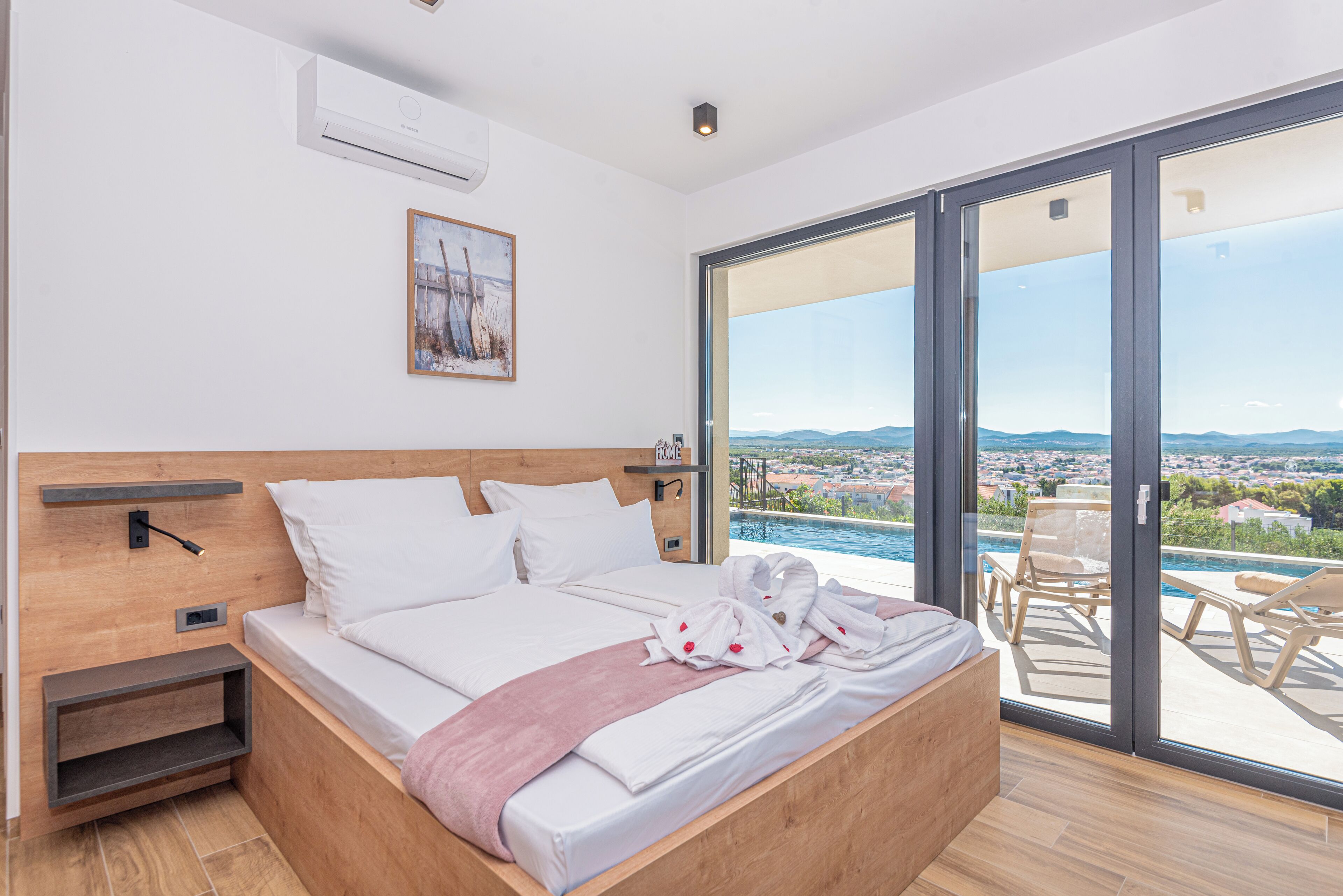A modern bedroom with a large bed, a view of the city, and a pool outside.