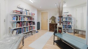 Ein gut beleuchteter Raum mit weißen Wänden, mehreren Bücherregalen voller Bücher, einer Holztür und einem kleinen Tisch mit einer Vase.