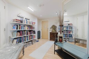 A well-lit room with white walls, multiple bookshelves filled with books, a wooden door, and a small table with a vase. - Eclectically Curated 2BD Flat in Canary Wharf (Greater London)