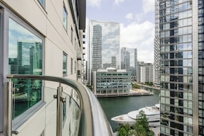 A high-rise building with a glass facade overlooking a river and a marina with boats. - Eclectically Curated 2BD Flat in Canary Wharf (Greater London)