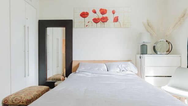 A bedroom with a bed, a nightstand, a chair, a dresser, a mirror, and a wall art piece. - Eclectically Curated 2BD Flat in Canary Wharf (Greater London)