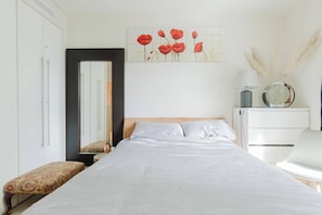 A bedroom with a bed, a nightstand, a chair, a dresser, a mirror, and a wall art piece.