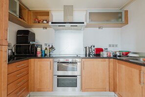 Une cuisine compacte dotée de meubles en bois, d’un four à micro-ondes, d’un four double et d’un plan de travail en acier inoxydable.