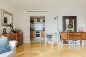 A modern kitchen with wooden cabinets, a dining area with a table and chairs, and a living room with a sofa and a decorative mirror.